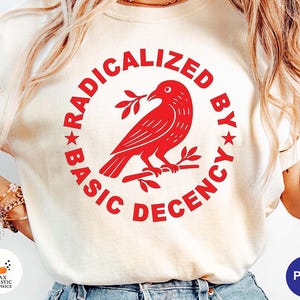 Peut inclure: Sweat-shirt crème avec un motif rouge. Le motif représente un oiseau perché sur une branche dans un cercle rouge, avec l'inscription "RADICALIZED BY BASIC DECENCY". Le t-shirt a des manches courtes.