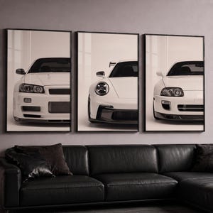 Puede incluir: Un conjunto de tres láminas de arte mural enmarcadas, cada una con la vista frontal de un coche deportivo blanco. La lámina de la izquierda muestra un Nissan Skyline GT-R, la central un Porsche 911 y la de la derecha un Toyota Supra.