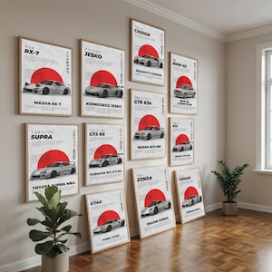 May include: A collection of ten rectangular wall posters featuring various sports cars, each displaying a large red circle, black text, and Japanese characters on a white background, arranged in a grid pattern on a light-coloured wall.