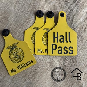 May include: Four yellow plastic livestock ear tags with black hardware. Three tags feature the black FFA emblem and the text Ms. Williams or Ms. W. One tag features the black text Hall Pass. Each tag has a circular hole at the top for attachment.