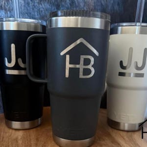 May include: Three insulated tumblers in black, charcoal, and white, each with a silver rim and base. The black tumbler has a handle and the initials "JJ" etched in silver. The charcoal tumbler features a house logo with "HB" in silver. The white tumbler also has "JJ".