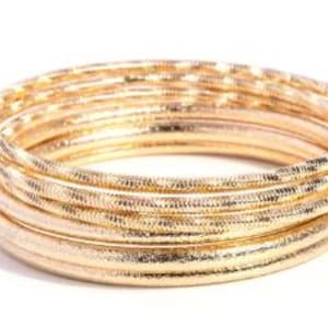 May include: A stack of gold-colored bangles with a textured surface. The bangles are arranged in a circular shape, with several bangles stacked together. The bangles have a shiny, metallic appearance.