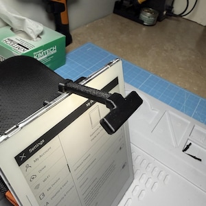 May include: A black tablet holder attached to a tablet, displaying a settings menu. The holder is made of a textured material and is positioned at an angle. A green box of Kimtech tissues is in the background.