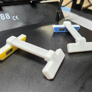 May include: Three white and yellow electronic components with a T-shaped design are arranged on a black surface. The components have a rectangular base with yellow and blue accents. The number "388 ce" is visible in the background.