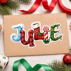 May include: A sticker featuring the name Julie spelled out in festive holiday motifs. The J is blue with snowflakes, the u and l are red plaid, the i is a red stocking, the e is a candy cane, and the final e is a green vine with lights.