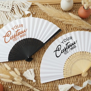 May include: Two white folding fans with custom text. One fan has a black handle, the other a natural wood handle. The fans are open, displaying vertical white and gray stripes. The text "YOUR Custom TEXT / IMAGE" is printed on each fan.