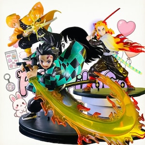 Peut inclure: Trois figurines de personnages d'anime Demon Slayer. Une figurine porte un haori à carreaux verts et noirs et manie une épée avec un effet de flamme jaune translucide. Une autre porte un haori jaune et la troisième a des cheveux en flammes.