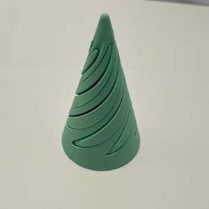 Puede incluir: Objeto decorativo en forma de cono verde claro con un diseño en espiral. El objeto tiene una base redondeada y se estrecha hasta un punto en la parte superior. El diseño en espiral crea una serie de líneas curvas que envuelven el cono.