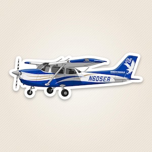 May include: A blue and white single-engine airplane sticker featuring the text N605ER on the fuselage and Embry-Riddle Aeronautical University on the tail. The design includes a white eagle graphic, the number 05, and gold accent stripes.