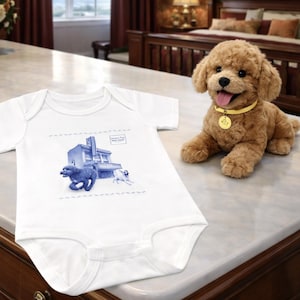May include: A white baby onesie with a blue illustration of two dogs running in front of a building. The text "Summer City, Little Island" is printed on the onesie. A plush brown dog with a yellow collar is next to the onesie.