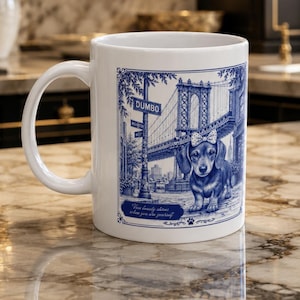May include: A white ceramic mug featuring a blue ink-style illustration of a dachshund wearing a polka-dot bow. The design includes the Manhattan Bridge, a DUMBO street sign, and the text, True beauty shines when you are yourself.