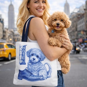 May include: A white tote bag with navy blue handles featuring a blue illustration of a puppy sitting on a shoe. The word "HOTEL" is printed vertically on the left side of the bag. A small brown dog is being held in the image.