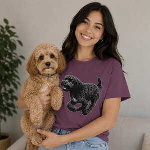 以下が含まれることがあります： プラム色の半袖Tシャツで、走っているポーズの黒い巻き毛の犬のグラフィックイラストが描かれています。このシャツはクルーネックで、無地の生地に犬の詳細なプリントが施されています。
