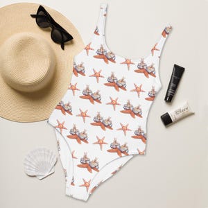 May include: White swimsuit featuring a pattern of orange starfish and sea creatures. The one-piece swimsuit has a scoop neck and is sleeveless. A sun hat, sunglasses, sunscreen, and a seashell are also visible.