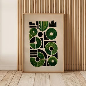 May include: Abstract art print in a wooden frame. The artwork features a geometric design with green and black shapes, including circles, rectangles, and curved lines, set against a beige background. The print is displayed on a wooden floor.