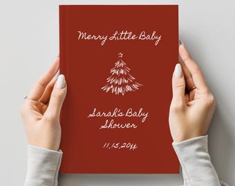 May include: A deep red hardcover book featuring white hand-lettered text that reads Merry Little Baby, Sarah's Baby Shower, and the date 11.15.20xx, centered above a white line-drawn illustration of a Christmas tree with a star on top.