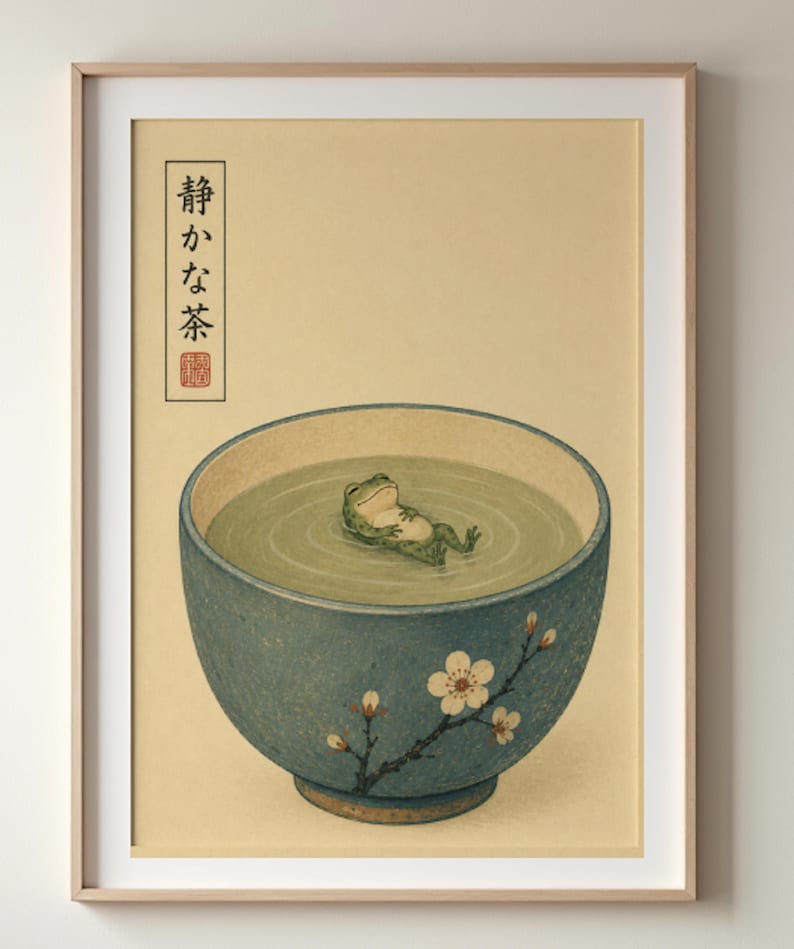 A framed vertical art print on a neutral wall shows a small frog floating in a large blue ceramic bowl of green liquid.
