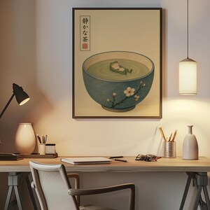 A framed frog illustration hangs above a wooden desk with a lamp, cup of pens, and white vase against a warm wall.