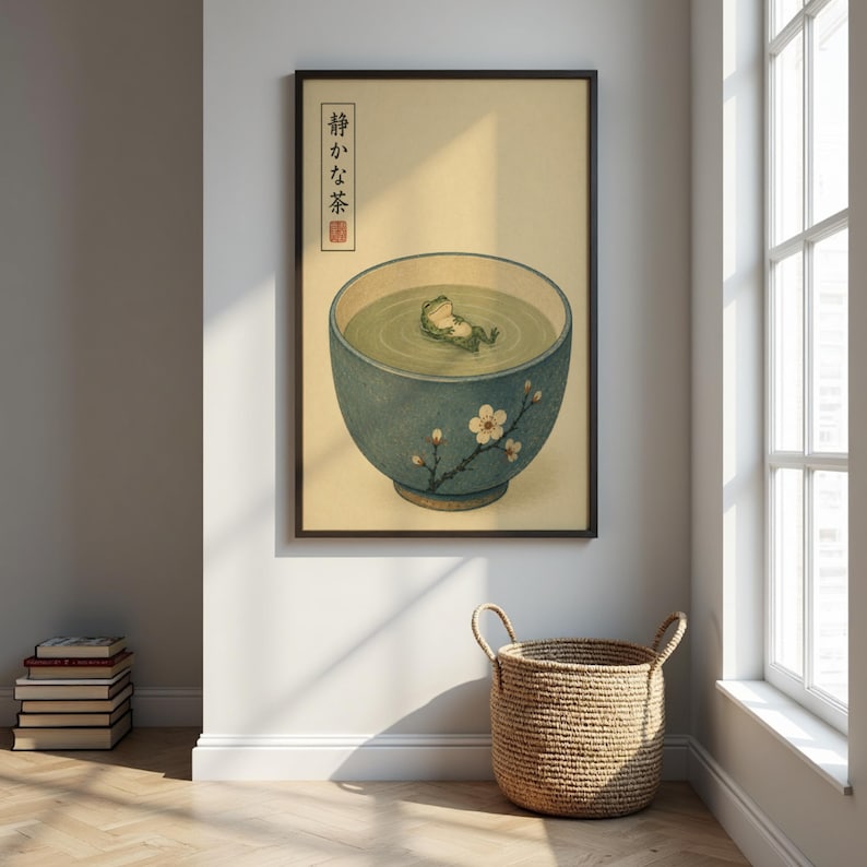 A framed botanical frog print hangs on a white wall next to a window, a woven basket, and a stack of books on the wooden floor.