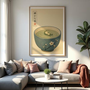 A framed art print hangs above a grey sectional sofa in a sunlit living room featuring a large potted plant and throw pillows.