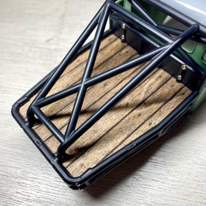 Peut inclure: Gros plan sur une maquette de benne de camion. La benne est compos&eacute;e de planches de bois et d'une cage de protection en m&eacute;tal noir. La benne est verte et grise.