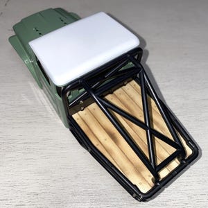 Peut inclure: Un petit camion vert olive avec un toit blanc et une benne &agrave; armature m&eacute;tallique noire. La benne a un design de planches de bois. Le camion est un jouet ou un mod&egrave;le, probablement pour l'affichage ou le jeu.