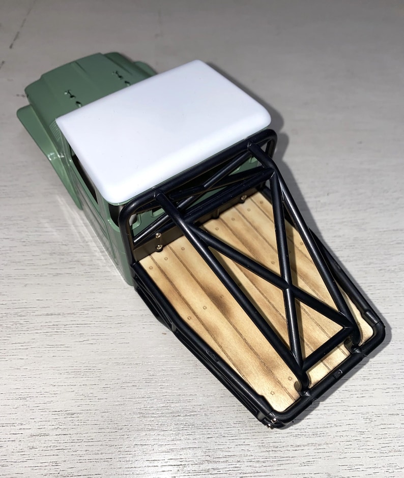 Peut inclure: Un petit camion vert olive avec un toit blanc et une benne &agrave; armature m&eacute;tallique noire. La benne a un design de planches de bois. Le camion est un jouet ou un mod&egrave;le, probablement pour l'affichage ou le jeu.