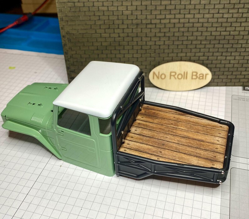 Peut inclure: Maquette d'un pick-up vert avec un toit blanc et une benne en bois. La benne est encadr&eacute;e de m&eacute;tal noir. Les mots "No Roll Bar" sont sur un panneau ovale en bois.