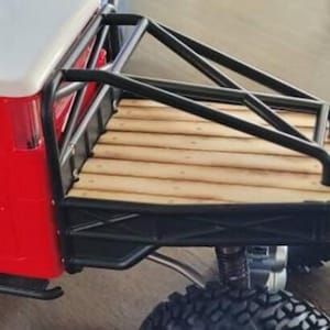 Peut inclure: Gros plan sur un camion jouet rouge et blanc avec une cage de protection noire et une benne en bois. Le camion est &eacute;quip&eacute; de gros pneus noirs tout-terrain et d'une suspension argent&eacute;e.