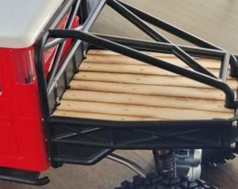 May include: A detailed view of a red and white toy truck with a black roll cage and a wooden bed. The truck has large, black off-road tires and a silver suspension system.