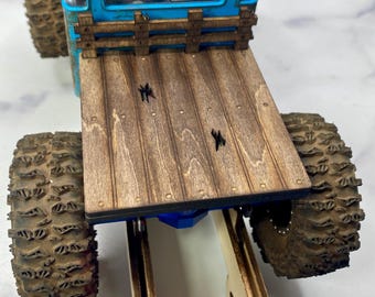 May include: A detailed model truck with a weathered, dark blue cab and a wooden flatbed. The truck features large, textured tires and the text "MOFOrc". The flatbed is made of wooden planks.