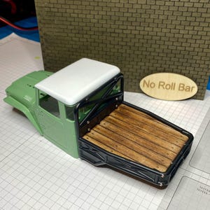 Peut inclure: Un mod&egrave;le r&eacute;duit de plateau de camion avec un lit en bois et un cadre noir. La cabine du camion est verte avec un toit blanc. Les mots "No Roll Bar" sont sur un ovale en bois.