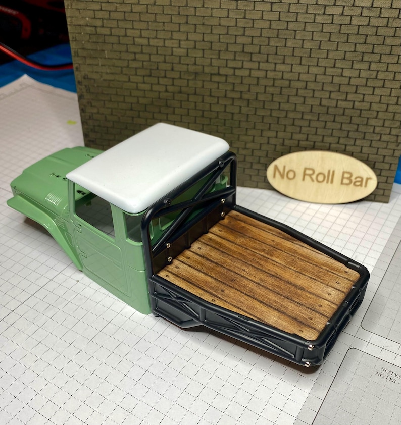 Peut inclure: Un mod&egrave;le r&eacute;duit de plateau de camion avec un lit en bois et un cadre noir. La cabine du camion est verte avec un toit blanc. Les mots "No Roll Bar" sont sur un ovale en bois.