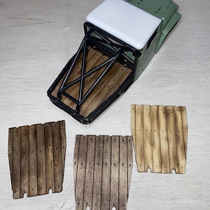 Peut inclure: Un mod&egrave;le r&eacute;duit de camion vert et blanc avec une benne &agrave; armature m&eacute;tallique noire et un plancher de benne en bois. Trois panneaux en bois avec des motifs de planches verticales sont affich&eacute;s en dessous du camion.