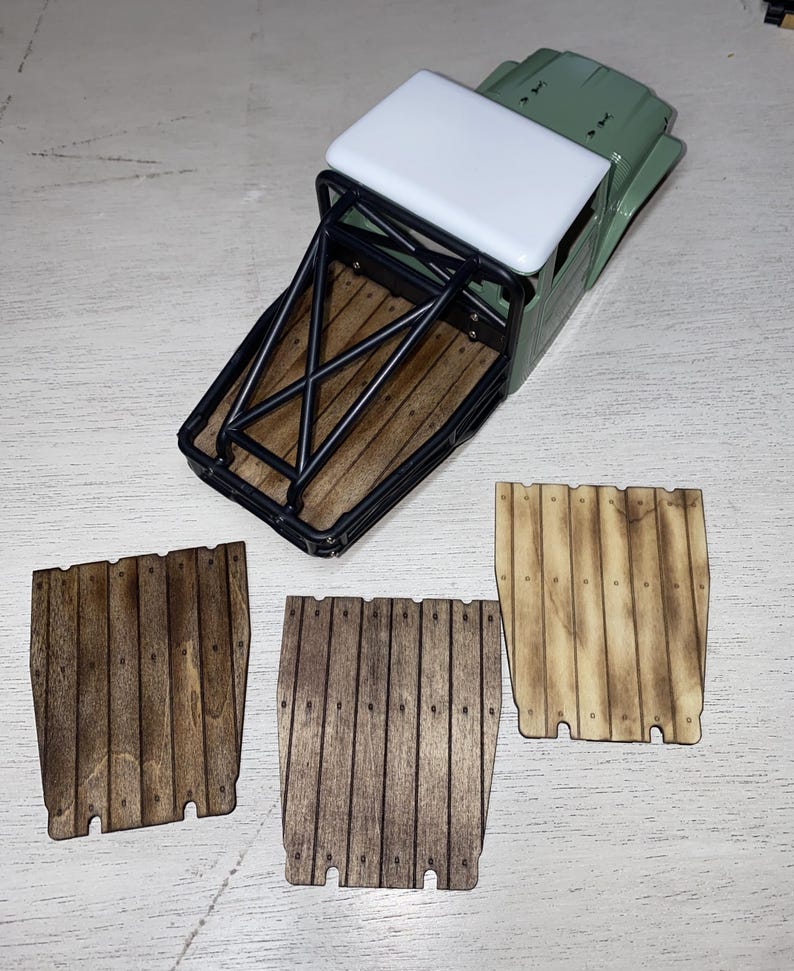 Peut inclure: Un mod&egrave;le r&eacute;duit de camion vert et blanc avec une benne &agrave; armature m&eacute;tallique noire et un plancher de benne en bois. Trois panneaux en bois avec des motifs de planches verticales sont affich&eacute;s en dessous du camion.