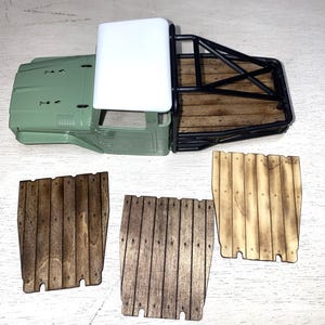 Peut inclure: Une carrosserie de camion mod&egrave;le vert olive avec un toit blanc, une cage de protection noire et un plateau en bois. Trois panneaux en bois avec des planches verticales sont &eacute;galement pr&eacute;sents, pr&eacute;sentant diff&eacute;rentes teintes de bois. Mod&egrave;le de loisir.