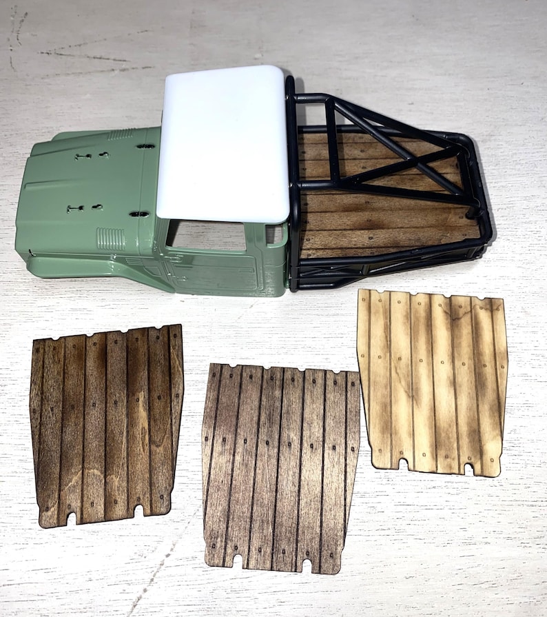 Peut inclure: Une carrosserie de camion mod&egrave;le vert olive avec un toit blanc, une cage de protection noire et un plateau en bois. Trois panneaux en bois avec des planches verticales sont &eacute;galement pr&eacute;sents, pr&eacute;sentant diff&eacute;rentes teintes de bois. Mod&egrave;le de loisir.