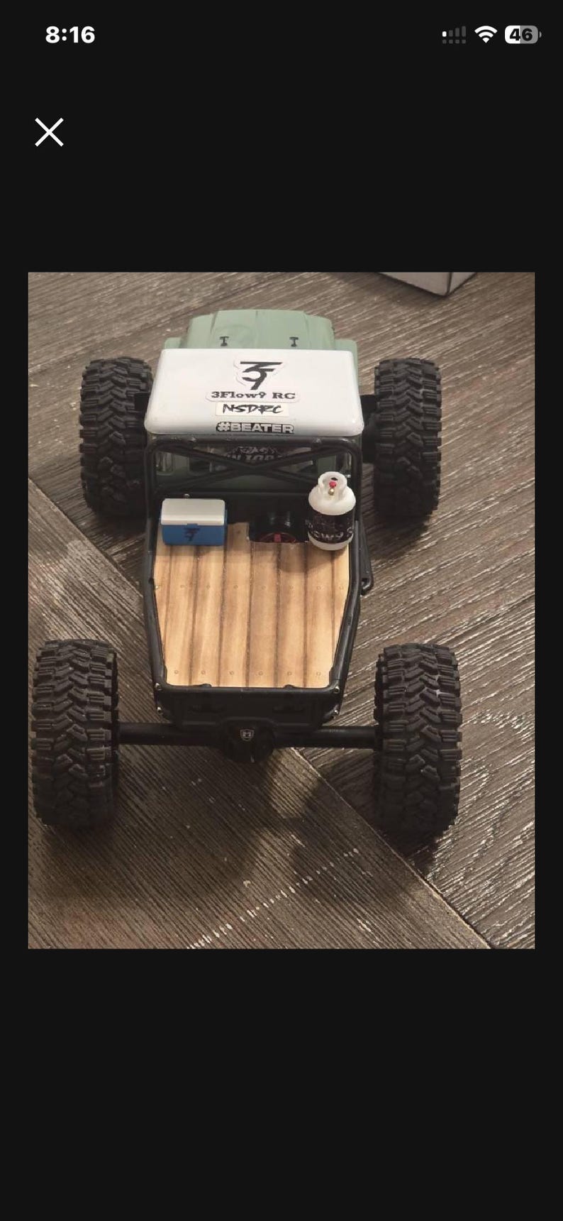May include: A green remote-controlled truck with a white roof featuring the text 3FLOW9 RC, NSDRC, and #BEATER. The truck bed has a wood-grain floor, a small blue and white cooler, and a miniature white propane tank with black text.