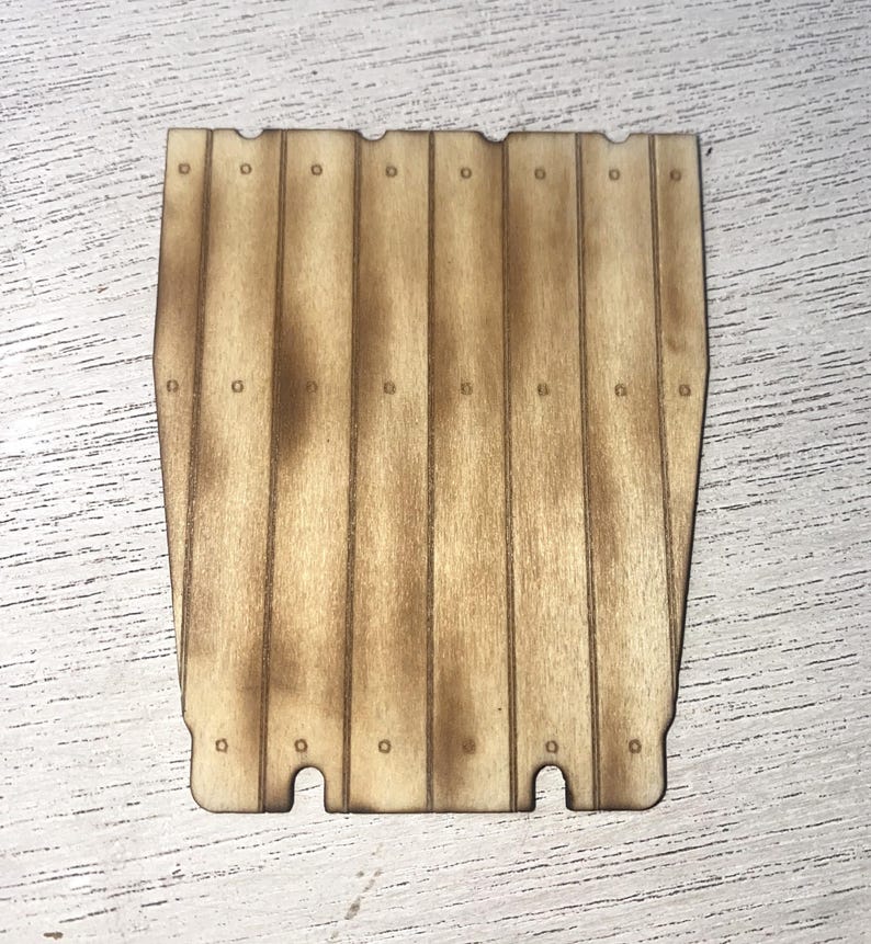 Peut inclure: Une pi&egrave;ce en bois d&eacute;coup&eacute;e au laser, ressemblant &agrave; une section de cl&ocirc;ture en bois. Le bois clair pr&eacute;sente des bords et des d&eacute;tails plus fonc&eacute;s, comme br&ucirc;l&eacute;s. De petits trous circulaires sont espac&eacute;s le long des planches de bois verticales. Environ 15 cm de large.