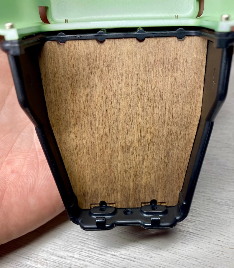 Peut inclure: Gros plan sur un petit conteneur rectangulaire ouvert. Le conteneur a un dessus vert clair et un cadre noir. L'int&eacute;rieur pr&eacute;sente un panneau en bois. Le conteneur est tenu par une main.