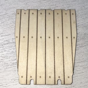 Peut inclure: Panneau en bois d&eacute;coup&eacute; au laser, compos&eacute; de planches verticales. Le panneau est de couleur brun clair et pr&eacute;sente de petits trous espac&eacute;s r&eacute;guli&egrave;rement en haut et au milieu de chaque planche. Le bas a deux d&eacute;coupes courbes.