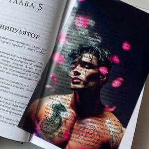 Peut inclure: Un livre ouvert au chapitre 5 intitulé Manipulator, avec une superposition en plastique translucide imprimée d'une image d'une personne torse nu tatouée, entourée d'icônes de cœurs roses flottants, posée sur le texte russe imprimé.