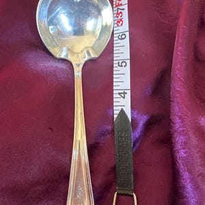 May include: A silver serving spoon with a heart-shaped bowl and ornate handle. The spoon is approximately 8 inches long. A black and white measuring tape is next to the spoon.