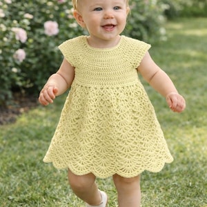 May include: A smiling baby wearing a yellow crochet dress and a matching headband. The dress has a scalloped hem and cap sleeves. The baby is wearing white shoes and walking on green grass.