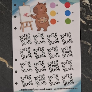 May include: A white rectangular planner insert featuring a cartoon capybara painting on an easel, a colour key with six circles, and sixteen black outline splat shapes. The text reads "Splat colour and save" and "LEE-ARNES CREATIONS FOR YOU".