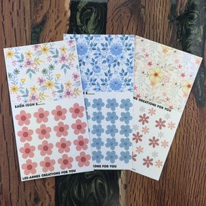 May include: Four sheets of floral stickers with diverse designs. One sheet displays pink flowers, another has blue flowers, and the others feature different floral patterns. The text "LEE-ARNES CREATIONS FOR YOU" is printed on the bottom of one sheet.