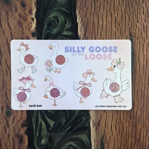 May include: A rectangular card with cartoon geese illustrations, each with glitter bellies and various accessories. The card features the text "Silly Goose on the Loose" and "Save £60". The card is set on a wooden surface.