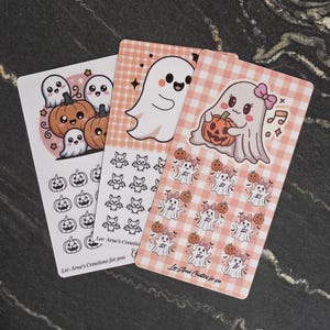 May include: Three rectangular sticker sheets featuring Halloween themes. Designs include cartoon ghosts, pumpkins, and bats with a pink gingham background on one sheet. Each sheet displays the text Lee-Arne's Creations for you at the bottom.