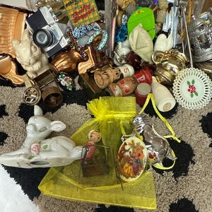 May include: A collection of assorted vintage trinkets including a miniature camera, a green box labeled Headquarters for Thrifty Shoppers, a ceramic deer, a yellow organza bag, a silver pig figurine, and various small decorative metal and ceramic items.