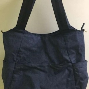 Peut inclure: Un sac fourre-tout bleu foncé avec deux poches extérieures et de longues bandoulières. Le sac est fait d'un matériau semblable au denim et a un design simple et fonctionnel. Le sac est accroché à un mur.
